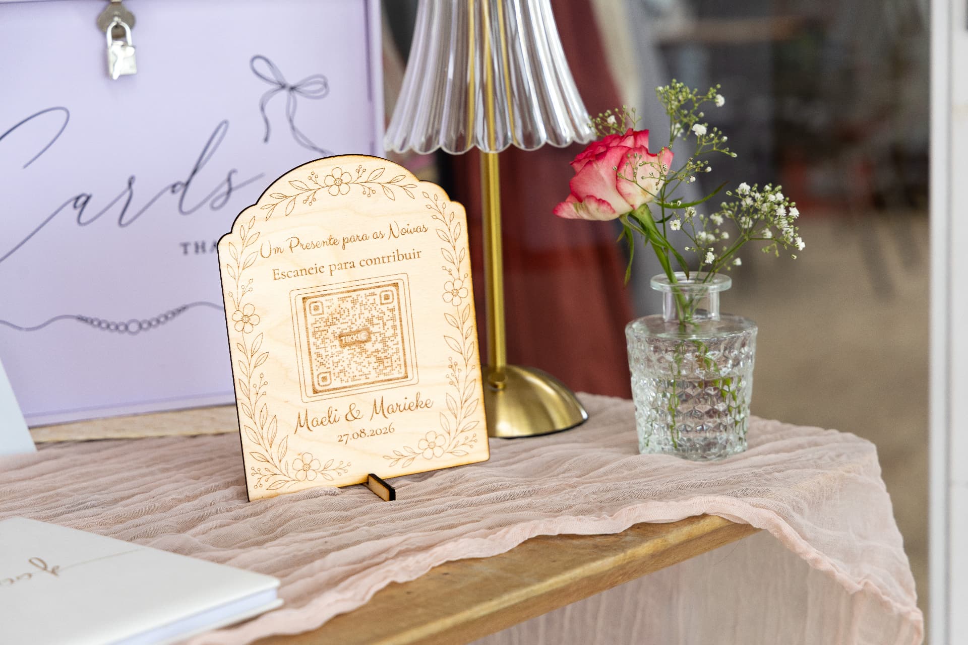 Engraved wooden sign with a QR code beside a rose in a cut glass vase