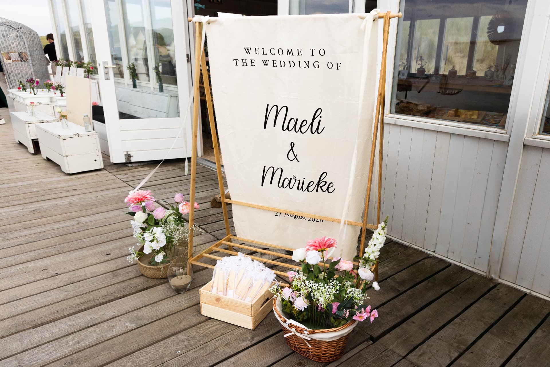 Canvas welcome sign on a wooden frame with floral arrangements at a beach wedding